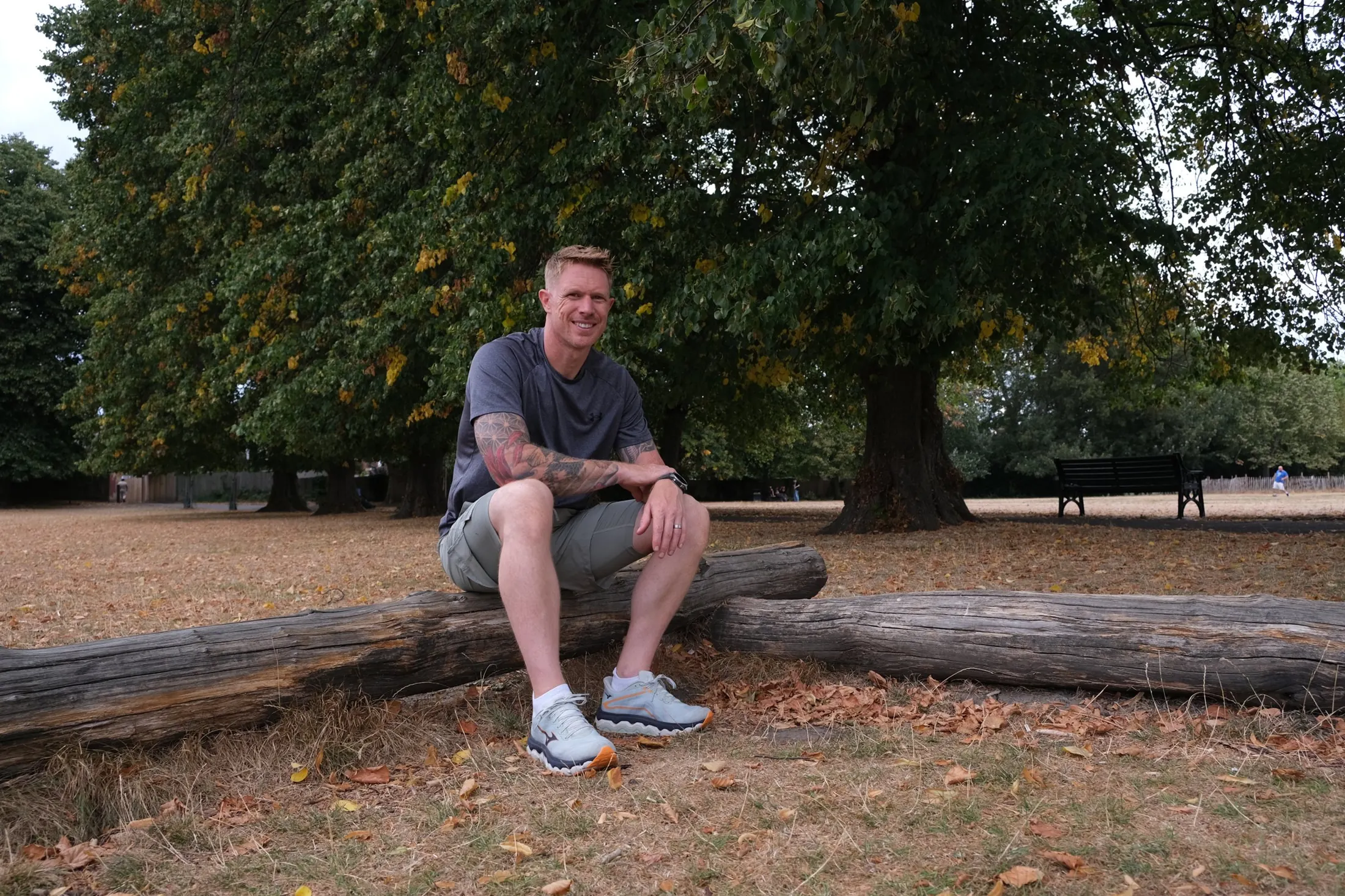 Mack Parnell smiling, sitting on a log in a park