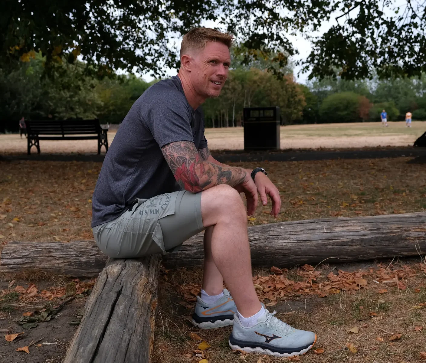 Mack Parnell smiling, sitting on a log in Lloyd Park, Walthamstow